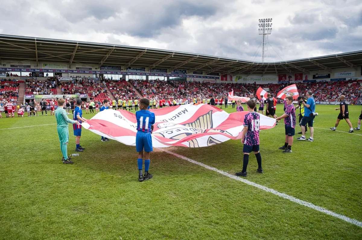 Children and players holding the matchday flag on the pitch before an Evestrust Legends Game.