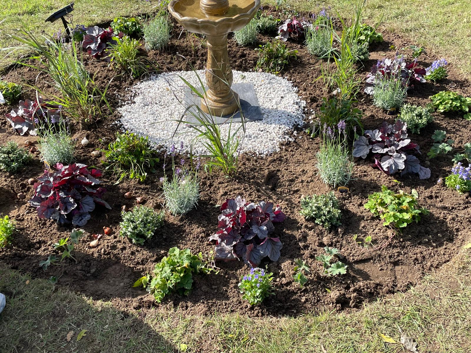 Plants and flowers around the white-stone base of the garden fountain.