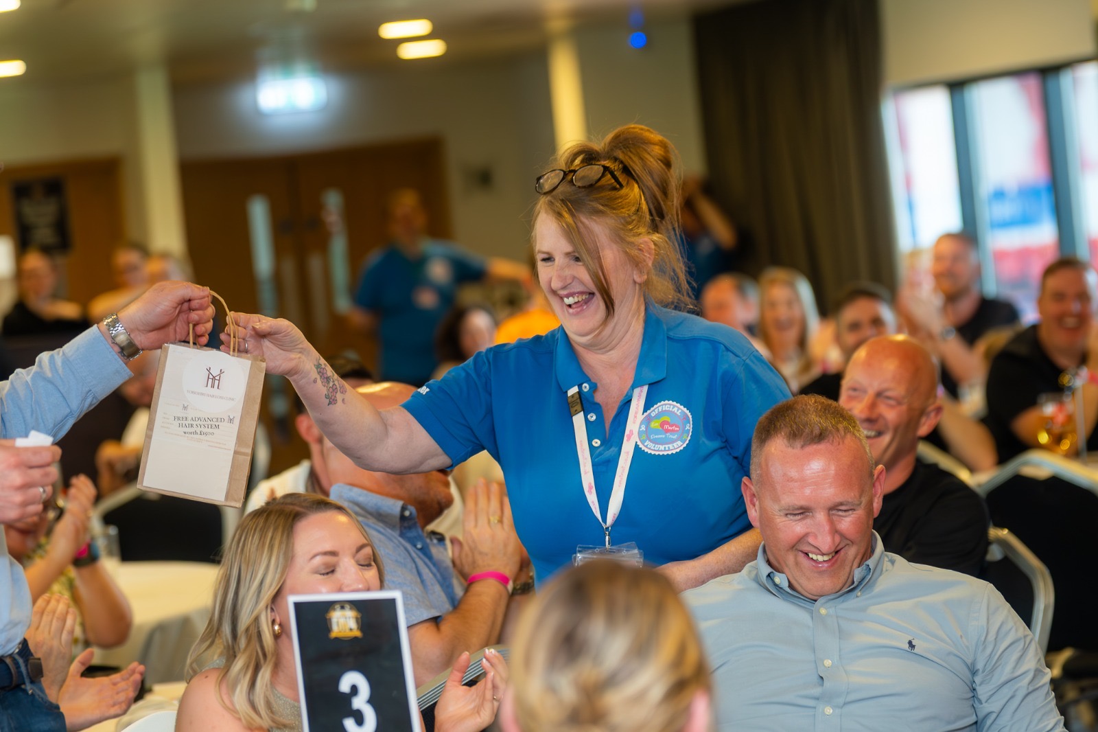 An Evestrust volunteer with a prize bag as people applaud at a fundraising gathering.